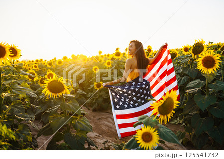 Woman proudly hold waving american USA flag in in the sunflower field. Independence Day, 4th July. Woman proudly hold waving american USA flag in in the sunflower field. Independence Day, 4th July. 125541732
