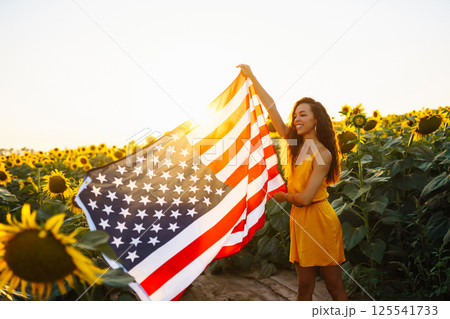 Woman proudly hold waving american USA flag in in the sunflower field. Independence Day, 4th July. Woman proudly hold waving american USA flag in in the sunflower field. Independence Day, 4th July. 125541733