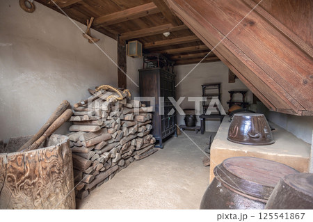 Traditional Korean storage room with stacked firewood wooden barrels shelves and earthenware jars under a rustic timber roof 125541867