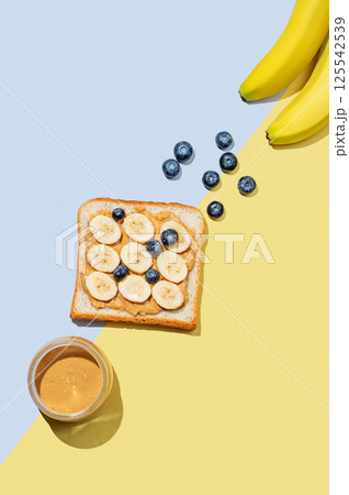 Peanut butter toast with banana, blueberry and nuts on a blue yellow background. 125542539