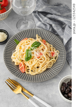 Creamy spaghetti with cherry tomatoes, parmesan cheese and basil on a plate on a light background 125542549