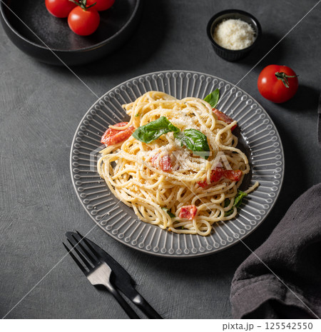 Creamy spaghetti with cherry tomatoes, parmesan cheese and basil on a plate on a dark background. Creamy spaghetti with cherry tomatoes, parmesan cheese and basil on a plate on a dark background. 125542550