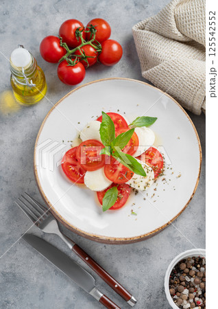 Caprese salad with sliced tomatoes, mozzarella and basil on a plate on a light background Caprese salad with sliced tomatoes, mozzarella and basil on a plate on a light background 125542552