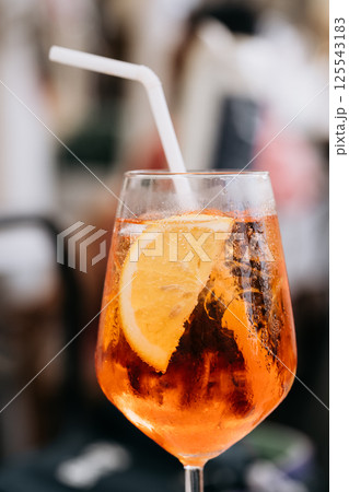 Glass of ice cold Aperol spritz cocktail served in a wine glass, decorated with slices of orange. Aperitive in street caffe in Italy 125543183