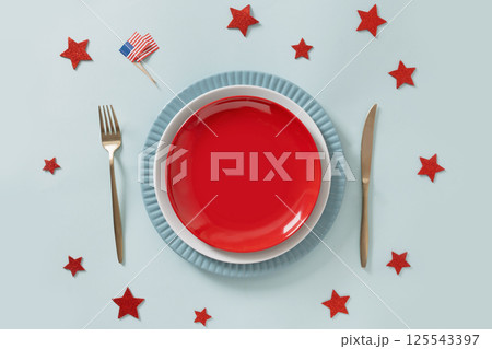 American table setting with stars for USA Independence Day. Festive dinner with empty plate and decoration in USA national flag on light blue background. View from above. 125543397