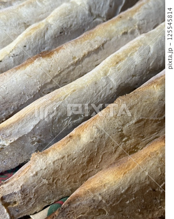 Golden-crusted loaves with crisp edges lie tightly packed, showing rustic cracks and texture from traditional baking on a patterned surface. Golden-crusted loaves with crisp edges lie tightly packed, showing rustic cracks and texture from traditional baking on a patterned surface. 125545814