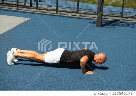 Athlete does push ups exercise and workout in public park. Outdoors training. Morning routine. Summer workout. 125546178
