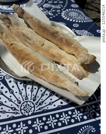 Three pieces of traditional flatbread rest on parchment over a metal tray, set atop a blue patterned tablecloth with cultural motifs, side view 125546214