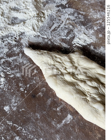 A hand-shaped piece of dough lies on a floured wooden surface, its wrinkled texture showing signs of preparation for traditional breadmaking. 125546216