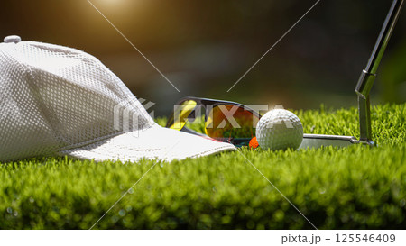 Golf ball on tee, white golf hat, sunglasses on the golf course 125546409