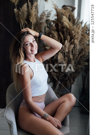 woman in light lingerie sitting on chair by window with flowers 125547719