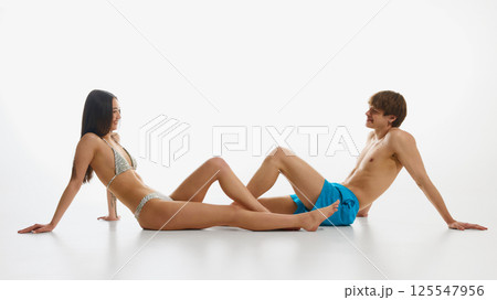 Happy, loving, smiling young man and woman, both in swimwear posing against white studio background. 125547956