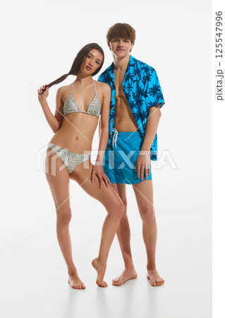 Charming young couple posing together dressed in tropical summer outfits, swimwear against white studio backwound. Charming young couple posing together dressed in tropical summer outfits, swimwear against white studio backwound. 125547996