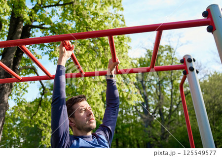 Man training on monkey bars in outdoor fitness park 125549577