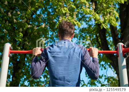 Man doing pull-ups on outdoor horizontal bar Man doing pull-ups on outdoor horizontal bar 125549579