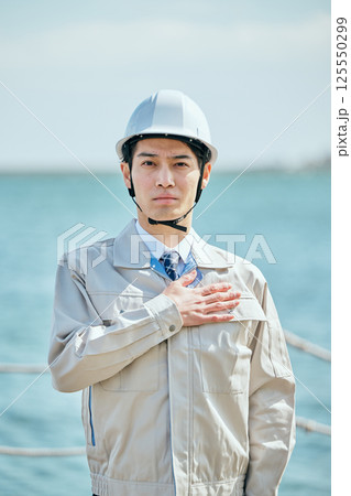 胸に手を当てる作業着姿の20代の若い男性 胸に手を当てる作業着姿の20代の若い男性 125550299