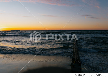 Ocean with waves, sunset sky is orange. water is choppy and waves are crashing on shore. 125550560