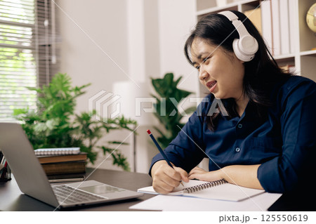 Happy student, studying for MBA exam, takes advantage of distance learning to attend school from home, balancing training and class. Woman studies book and research for online academy using laptop. 125550619