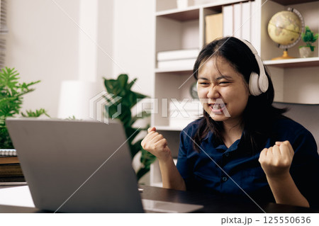 Happy student, studying for MBA exam, takes advantage of distance learning to attend school from home, balancing training and class. Woman studies book and research for online academy using laptop. 125550636