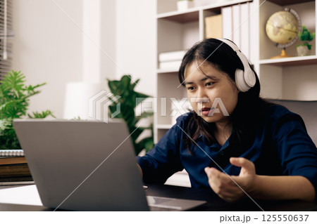 Happy student, studying for MBA exam, takes advantage of distance learning to attend school from home, balancing training and class. Woman studies book and research for online academy using laptop. 125550637