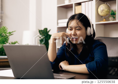Happy student, studying for MBA exam, takes advantage of distance learning to attend school from home, balancing training and class. Woman studies book and research for online academy using laptop. 125550638