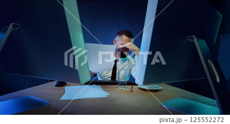 Frustrated businessman sitting in office, reading financial reports during severe collapse, working overtime under pressure. 125552272