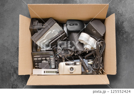 Old electronic devices in a cardboard box. The concept of recycling used gadgets. Black background Old electronic devices in a cardboard box. The concept of recycling used gadgets. Black background 125552424