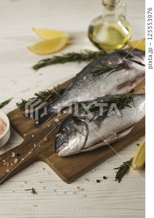Fresh dorado fish with lemon, rosemary and spices on wooden cutting board, close up 125553976