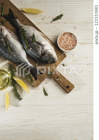 Fresh dorado fish with lemon, rosemary and spices on wooden cutting board, close up Fresh dorado fish with lemon, rosemary and spices on wooden cutting board, close up 125553981