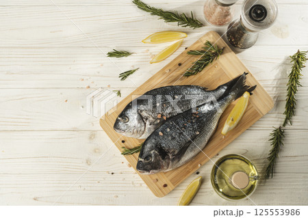 Fresh dorado fish with lemon, rosemary and spices on wooden cutting board, close up 125553986
