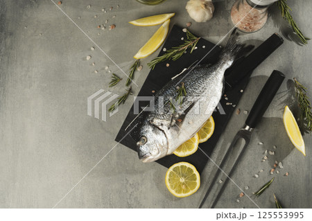 Fresh dorado fish with lemon, rosemary and spices on black cutting board, close up 125553995