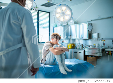 Depressed teenage patient sitting on hospital bed, waiting for doctor. 125554035