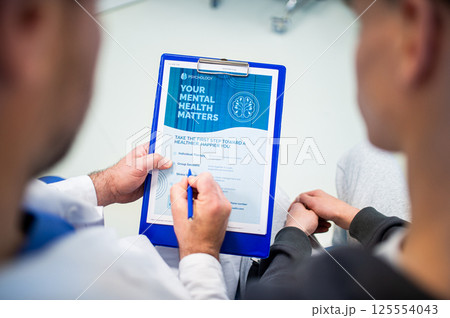 Close-up of doctor and teenage patient filling out mental health evaluation form. 125554043