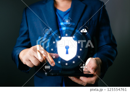 A professional interacts with a glowing shield icon on a tablet, symbolizing secure cyber systems designed to protect data, emphasizing innovation, safety, and advanced digital security. 125554761