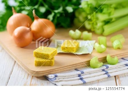 chicken bouillon cubes and fresh vegetables for soup on white wooden table, selective focus. chicken bouillon cubes and fresh vegetables for soup on white wooden table, selective focus. 125554774