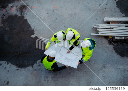 High angle view of engineers and construction workers reviewing blueprints, building site. 125556139