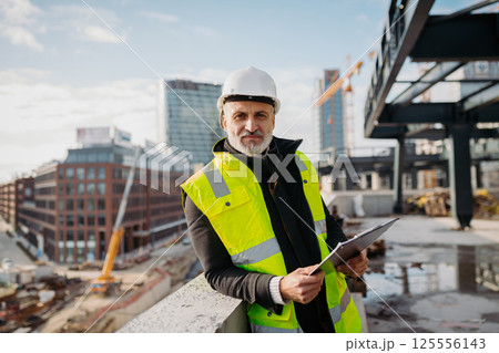 Engineer checking building documentation on clipboard at construction site. Engineer checking building documentation on clipboard at construction site. 125556143