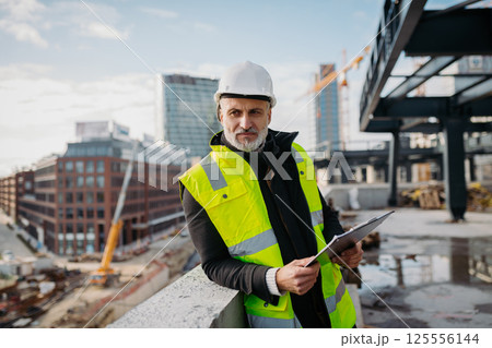 Engineer checking building documentation on clipboard at construction site. Engineer checking building documentation on clipboard at construction site. 125556144
