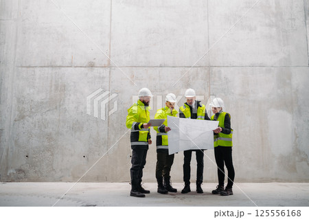 Team of engineers and construction workers reviewing blueprints, building site. 125556168