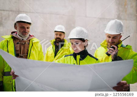 Team of engineers and construction workers reviewing blueprints, building site. Team of engineers and construction workers reviewing blueprints, building site. 125556169