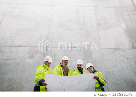 Team of engineers and construction workers reviewing blueprints, building site. 125556179