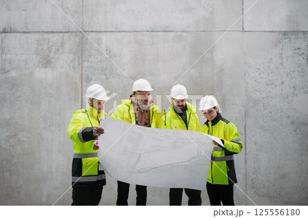 Team of engineers and construction workers reviewing blueprints, building site. 125556180