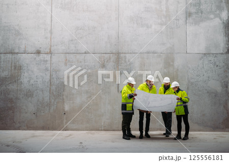 Team of engineers and construction workers reviewing blueprints, building site. 125556181