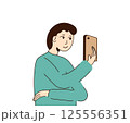 Young man holding the phone in his hand in front of his face and looking at smartphone. Boy looks at his phone screen. Men stands and talks on video call. Takes pictures. Vector illustration. 125556351