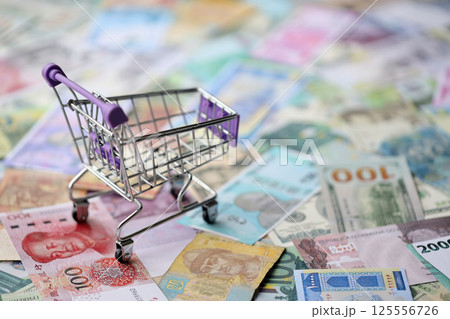 Supermarket trolley on many banknotes of different currency. Background of shopping worldwide Supermarket trolley on many banknotes of different currency. Background of shopping worldwide 125556726