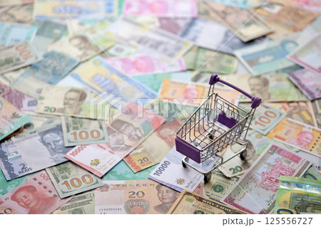 Supermarket trolley on many banknotes of different currency. Background of shopping worldwide 125556727