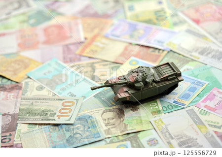 Small green tank on many banknotes of different currency. Background of war funding 125556729