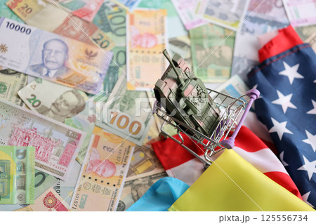 Toy tank on US flag and ukrainian flag on many banknotes of different currency 125556734