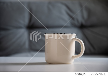 White mug on white table at home interior in living room. Beverage. Mockup. Perfect for businesses selling mugs, overlay your design on to image. White mug on white table at home interior in living room. Beverage. Mockup. Perfect for businesses selling mugs, overlay your design on to image. 125557024