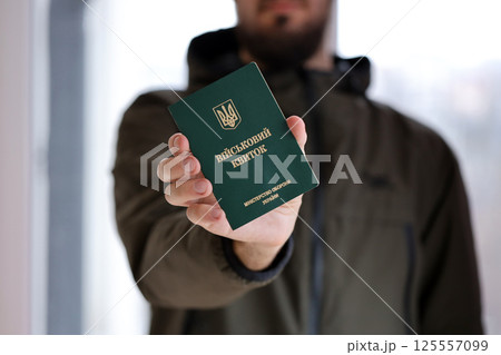 Young ukrainian conscript soldier shows his military token or army ID ticket indoors 125557099